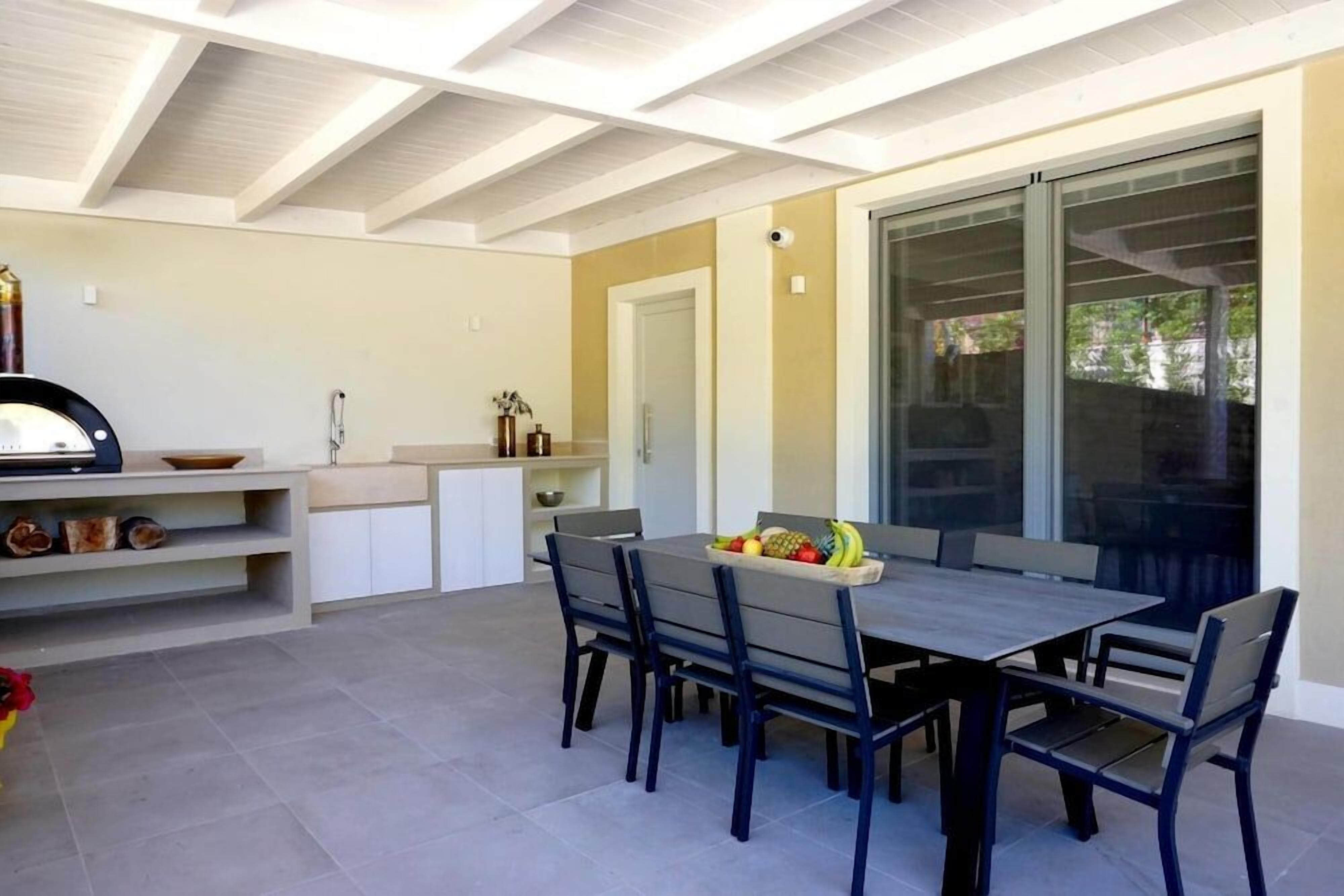 Un área de comedor exterior con una mesa y sillas, una barra de cocina integrada y un puerta corrediza de vidrio que da a un patio.