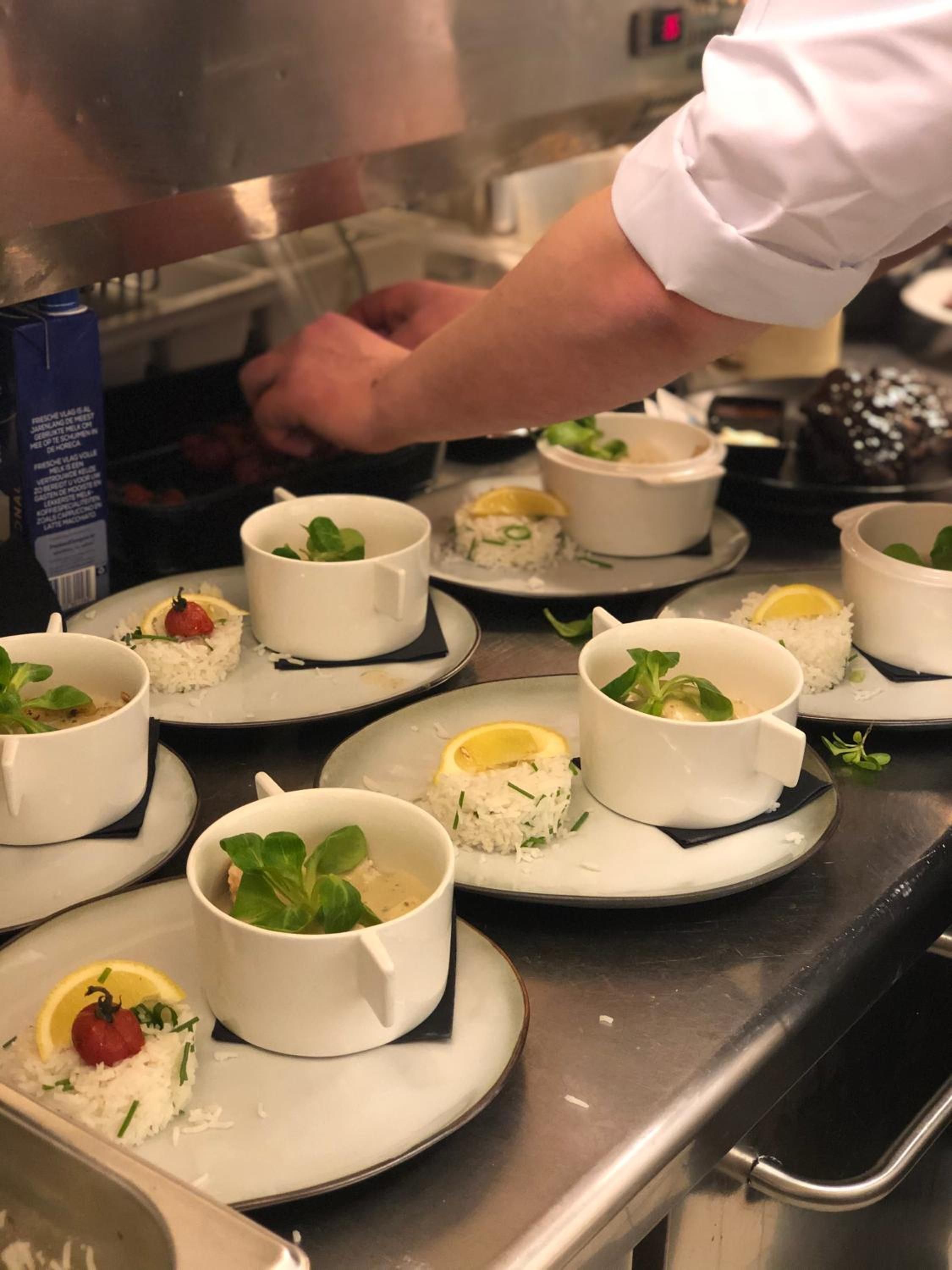 A chef preparing food in a kitchen with white bowls containing rice and garnishes on plates.