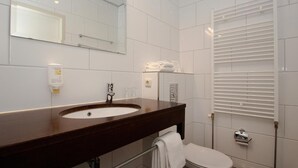 Un baño moderno con tocador de madera oscura, un lavabo blanco, un espejo, un inodoro y un perchero blanco para toallas.