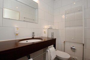Casa de banho moderna com toucador em madeira escura, uma sanita, um espelho e um porta-toalhas branco.