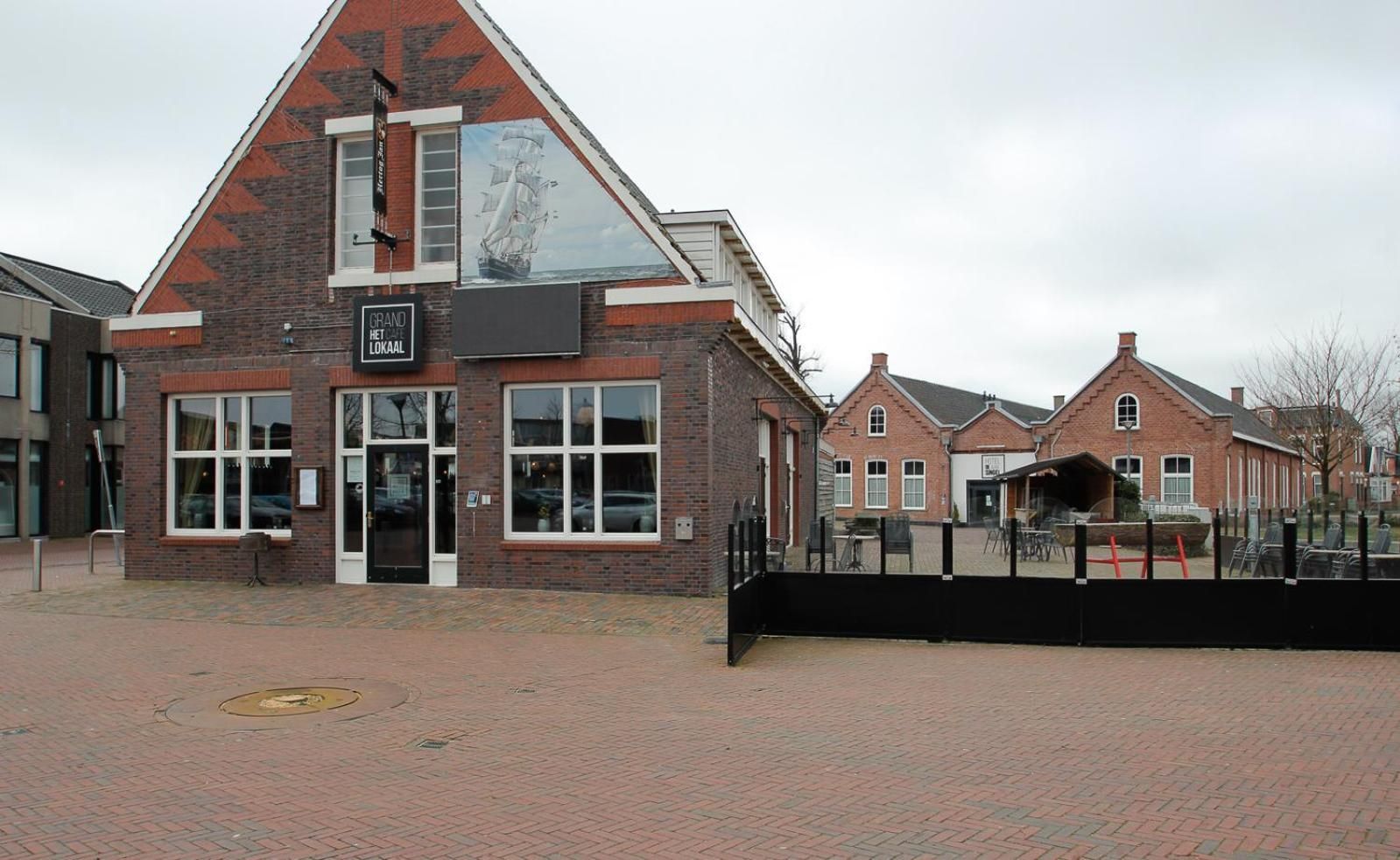 Een bakstenen gebouw met een groot raam en een bord waarop staat 'GRAND HET LOKAAL'.