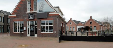A brick building with a large window and a sign that reads 'GRAND HET LOKAAL'.