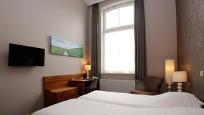 Una habitación de hotel con cama, escritorio, silla, televisor y ventana con cortinas.