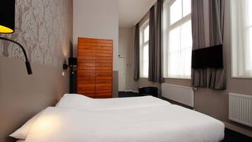 Ein Hotelzimmer mit einem Bett, einem Kleiderschrank, einem Schreibtisch, einem Stuhl, einem Fernseher und einem Fenster mit Vorhängen.