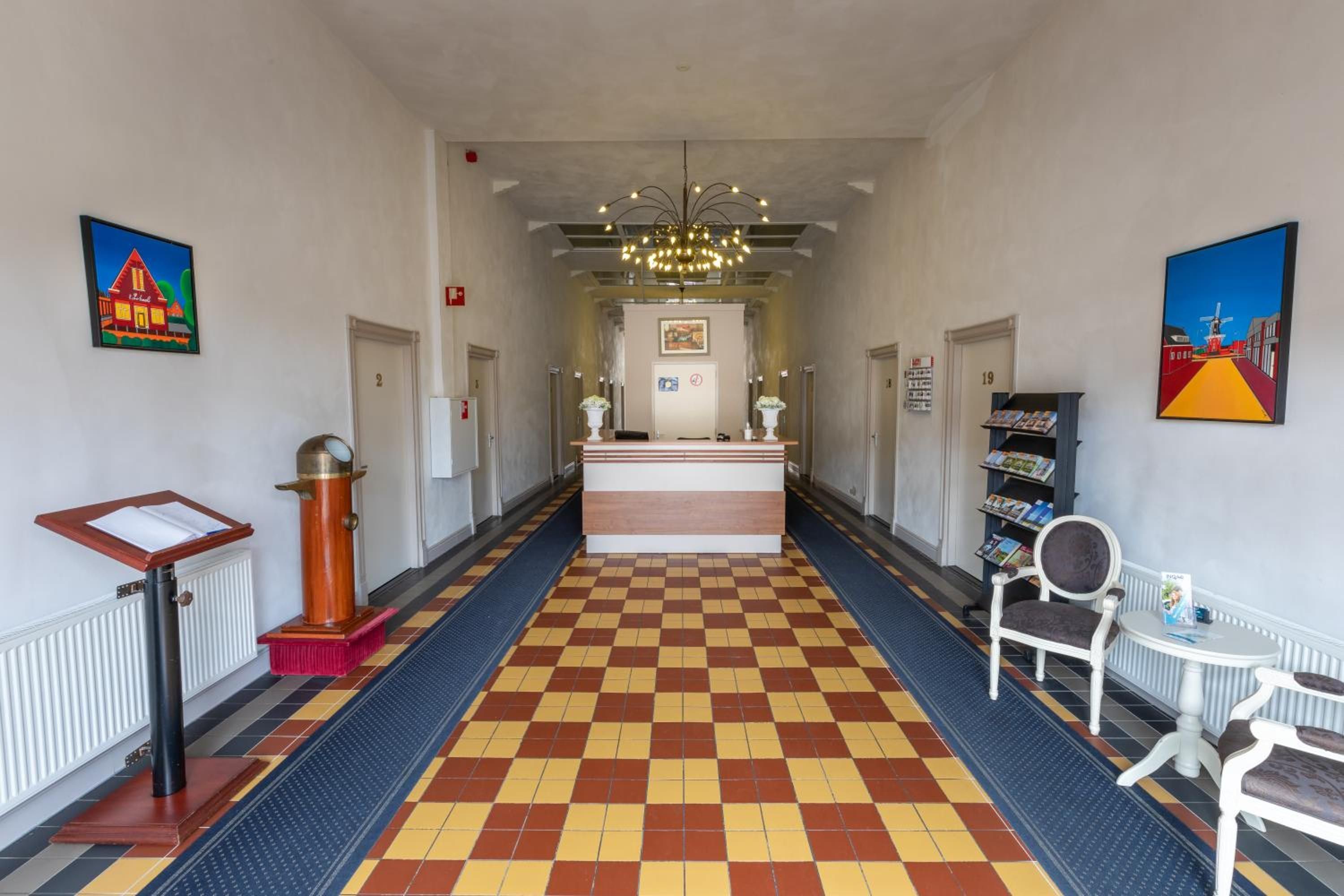 Un vestíbul d'hotel amb un taulell d'enregistrament, una recepció, una zona d'espera, una zona de seients amb una cadira, una taula petita i una prestatgeria.