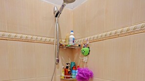 A shower with a handheld showerhead, a blue bucket, and a shelf with toiletries. - Spot On 92167 Jodoh Stay Syariah (Batam)