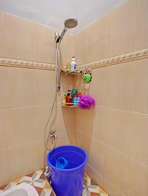 A shower with a handheld showerhead, a blue bucket, and a shelf with toiletries. - Spot On 92167 Jodoh Stay Syariah (Batam)