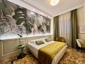 A hotel room with a large bed, a green armchair, a small table, and a wall with a leaf pattern. - Hotel Bellonda (Forte dei Marmi)