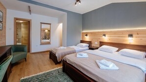 Quarto de hotel com duas camas, uma cabeceira de madeira, uma poltrona verde, uma escrivaninha pequena e um espelho.
