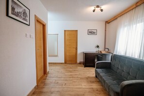 Un pasillo con suelo de madera, un sofá, un escritorio con una planta y una puerta.
