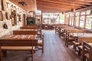 Un interior rústico con bancos y mesas de madera, paredes de piedra y ventanas amplias.