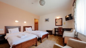 Quarto de hotel com duas camas, uma mesa, uma cadeira, televisão e janela com cortinas.