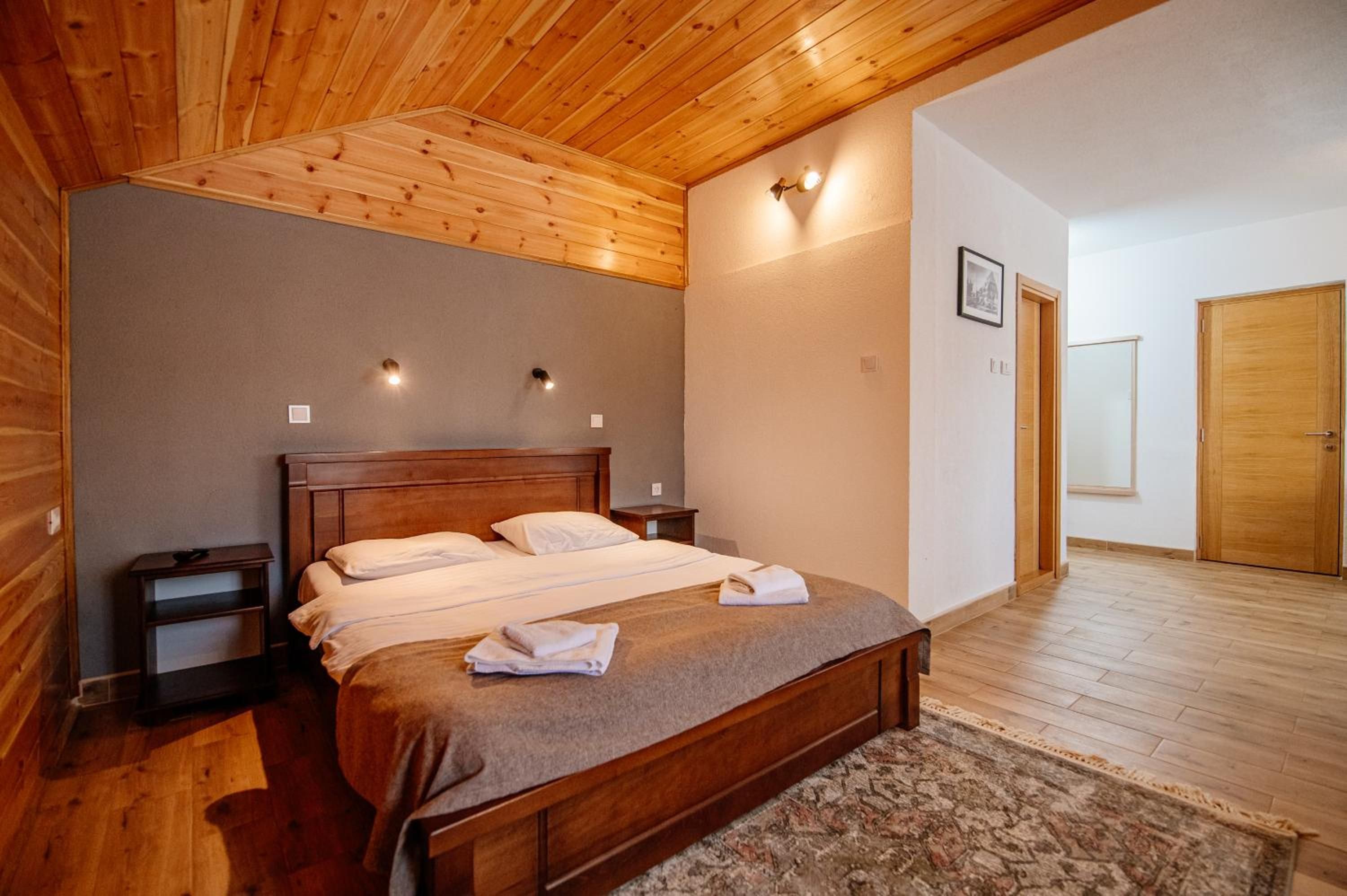 A bedroom with a wooden ceiling, a bed with a grey bedspread, two bedside tables, and a nightstand.