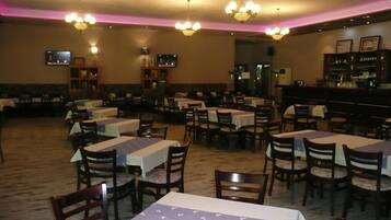 Un restaurante con varias mesas y sillas, una zona de bar y lámparas de techo.