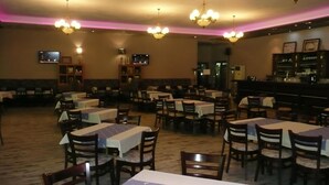 Un restaurante con varias mesas y sillas, una zona de bar y lámparas de techo.