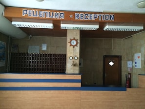 Una zona de recepción con un cartel que dice 'PELEPENIA RECEPTION' y un reloj en la pared.