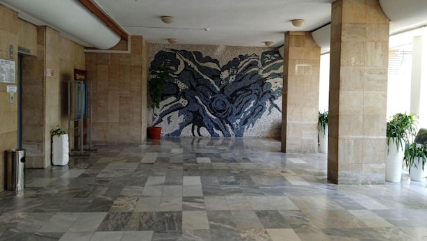 Un lobby amplio con un papel tapiz estampado, piso de baldosas y plantas en macetas.