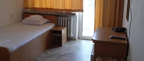 A hotel room with two single beds, a small desk with a chair, a radiator, and a window with curtains.