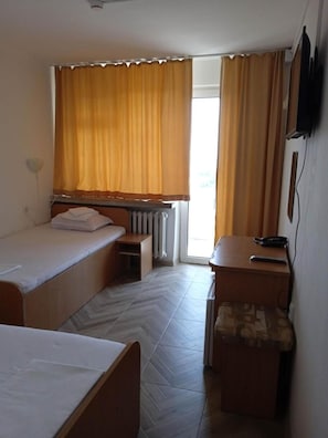 Habitación de hotel con dos camas individuales, un escritorio pequeño con una silla, un radiador y una ventana con cortinas.