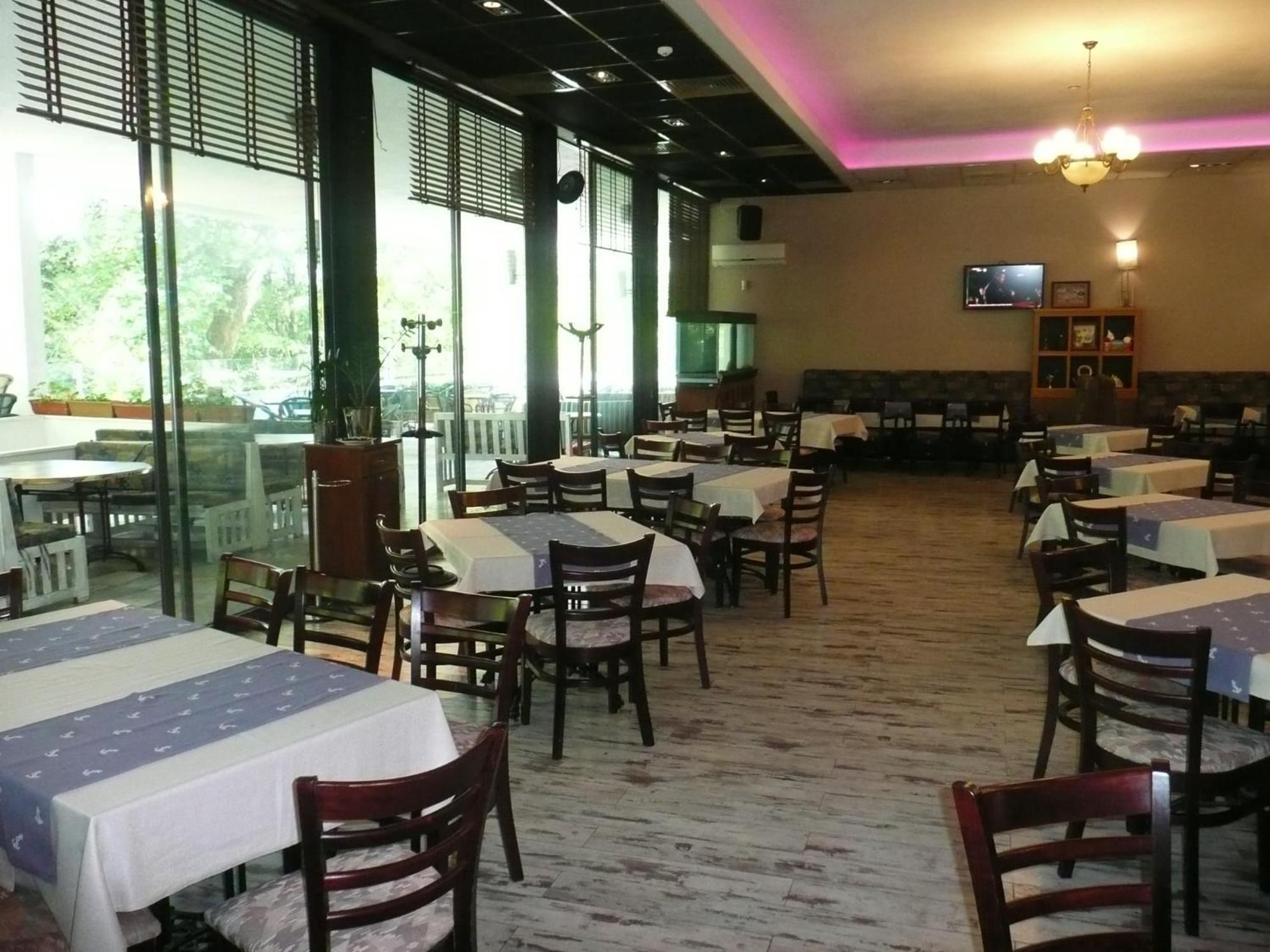 A restaurant with multiple tables and chairs, large windows, and a television on the wall.