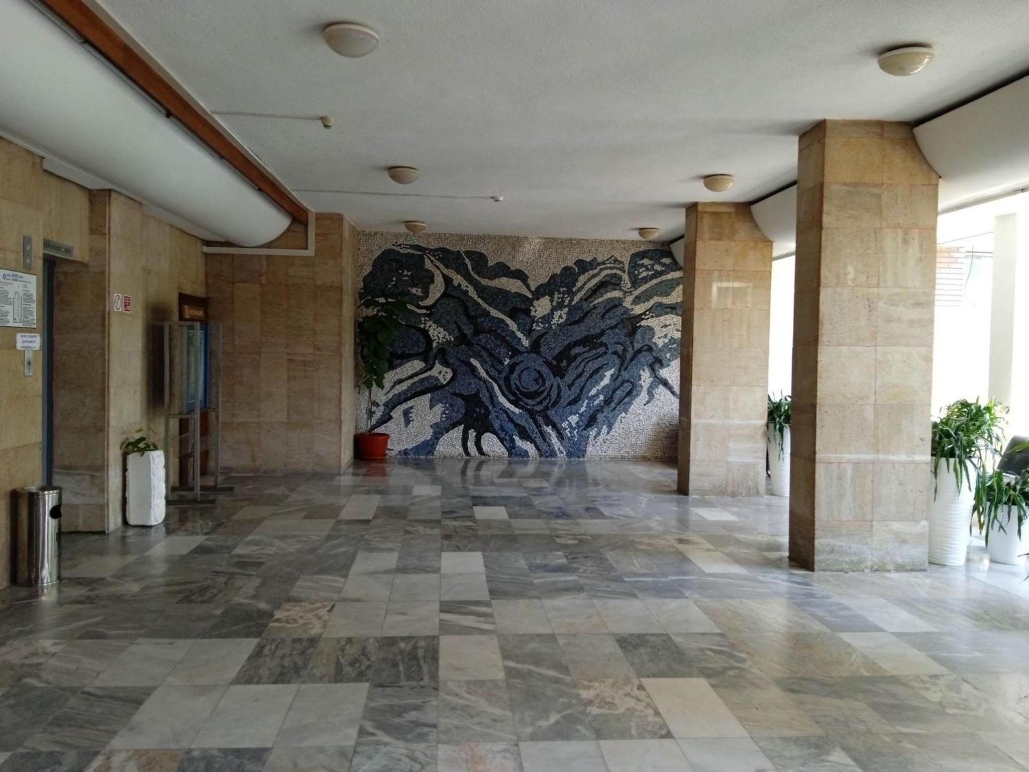Un'ampia hall con parete decorata, pavimento piastrellato e piante in vaso.