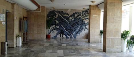 A spacious lobby with a patterned wall, tiled flooring, and potted plants.