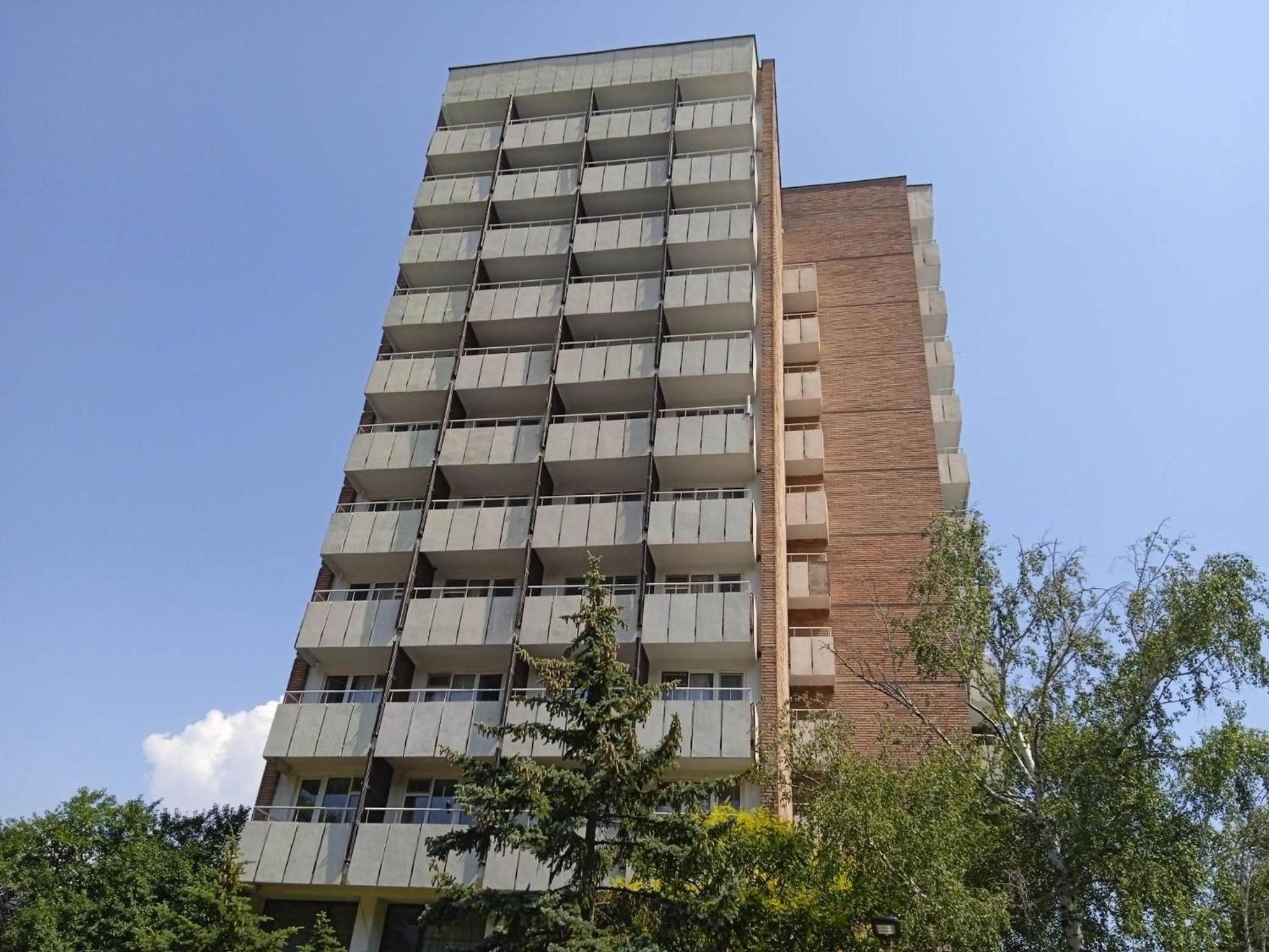 A multi-story building with balconies, a brick facade, and surrounding greenery.