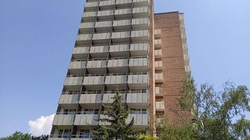Un edificio de varios pisos con balcones, fachada de ladrillo y vegetación circundante.