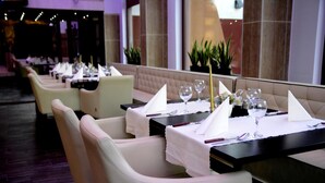 A restaurant with neatly arranged tables, each with a white tablecloth, wine glasses, and cutlery. - Hotel Minerva (Mosonmagyarovar)
