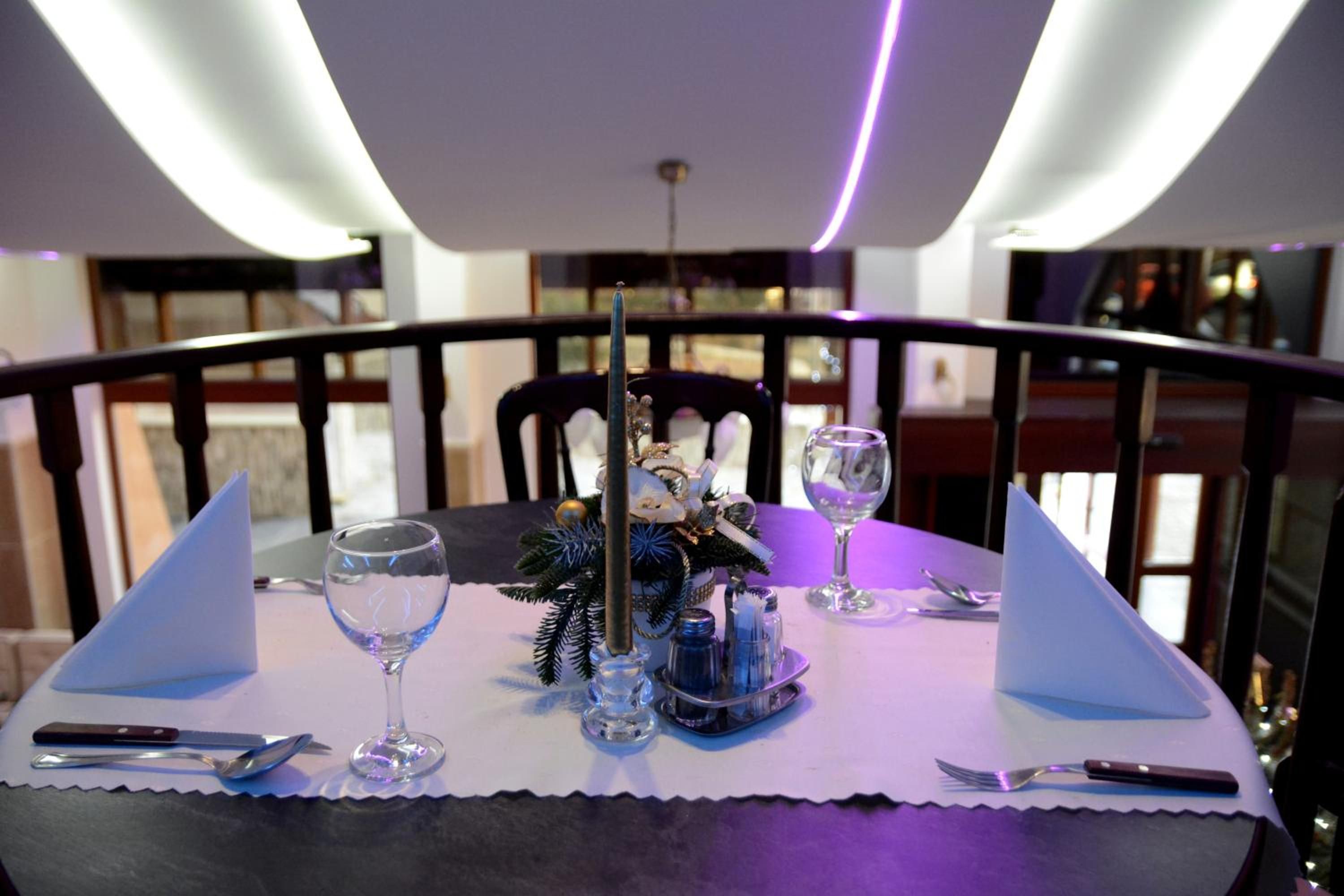 Una mesa de comedor preparada con una vela, saleros y pimenteros, una copa y cubiertos.