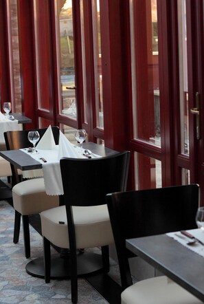 Un comedor interior con mesas y sillas, ventanas amplias y vistas al exterior.