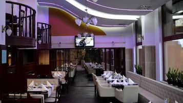 A restaurant with a modern interior, including a balcony with wooden railings and a television mounted on the wall.