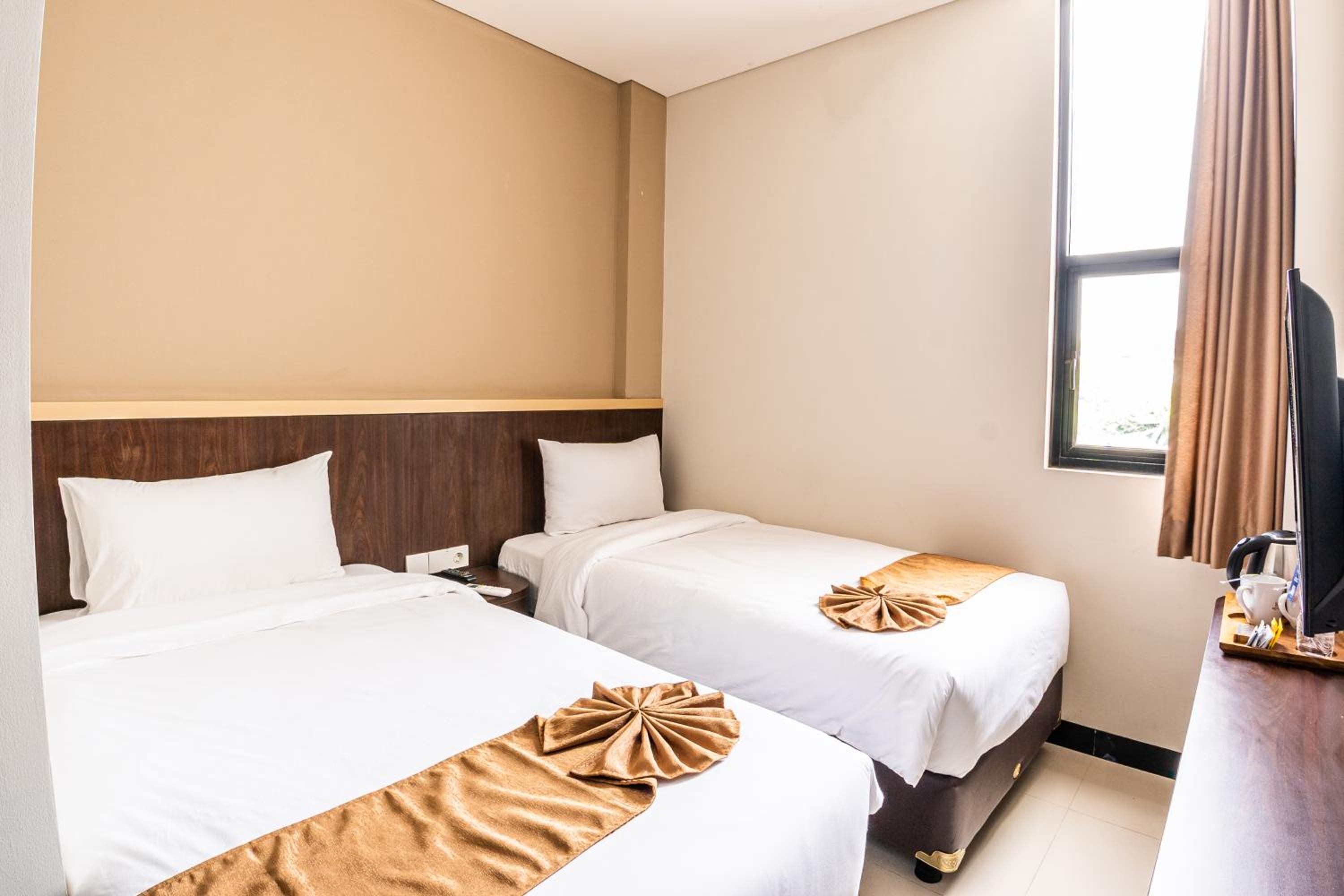 A hotel room with two beds, a wooden headboard, a TV, and a window with curtains.