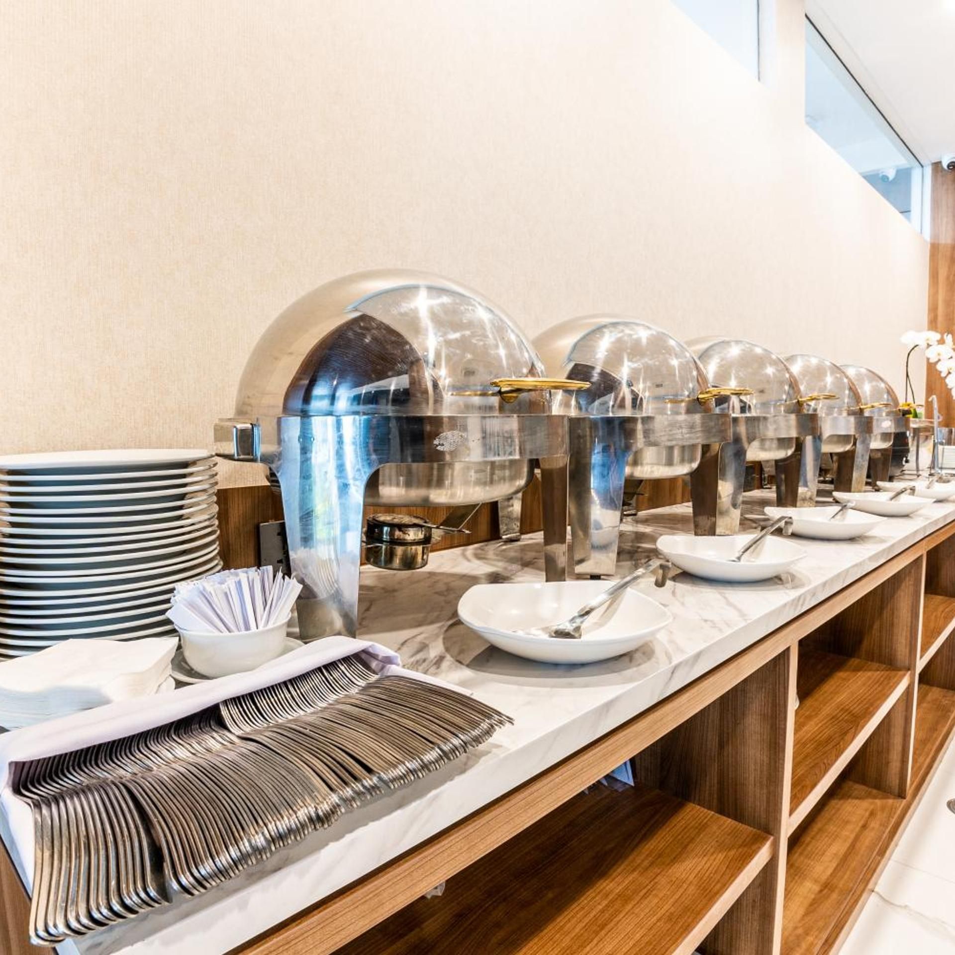 A buffet setup with multiple serving stations, including clear glass dome covers over food containers, white plates, and silverware.
