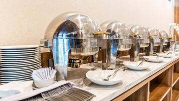 A buffet setup with multiple serving stations, including clear glass dome covers over food containers, white plates, and silverware.