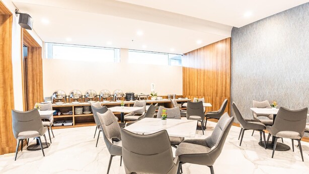 Un comedor moderno con mesas redondas y sillas grises, un panel de pared de madera y un suelo de mármol.