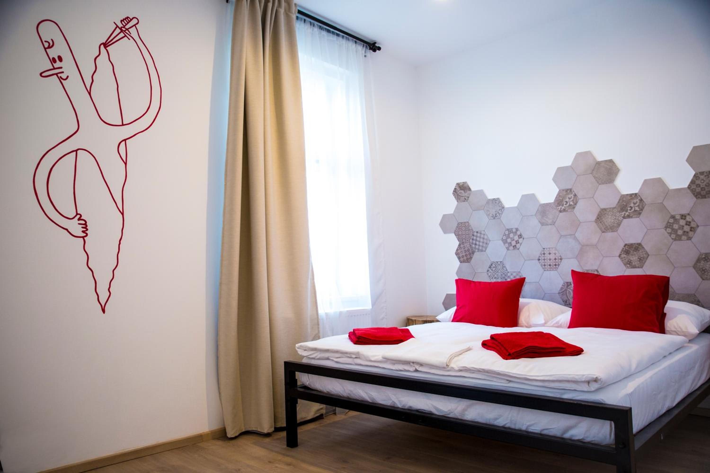 Ein Schlafzimmer mit einem Bett, einem Fenster mit Vorhängen, einer Wand mit geometrischem Muster und einer Wand mit einer Linienzeichnung.