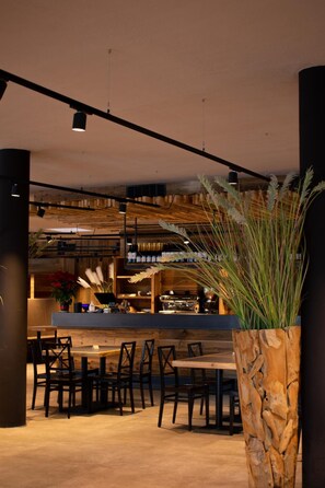 A modern interior with a wooden dining area, a bar with bottles, and a large potted plant. - Hotel Leonard (Nova Ponente)