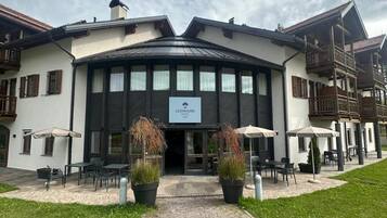 Ein Hotel mit zentralem Eingang, Außenbereich mit Sitzgelegenheiten und einem gepflasterten Weg zum Eingang.