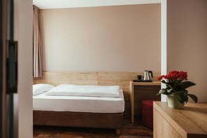 A hotel room with a bed, a small bedside table, a red ottoman, and a potted plant. - Hotel Leonard (Nova Ponente)