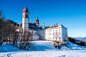 A historic building with a prominent tower and multiple spires, surrounded by snow-covered landscape and trees. - Hotel Leonard (Nova Ponente)
