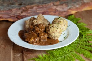 A plate with meatballs and gravy, a wooden table, and a green fern. - Hotel Leonard (Nova Ponente)