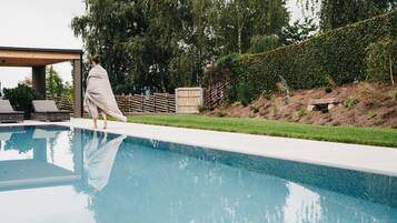 A swimming pool with a wooden deck and lounge chairs.