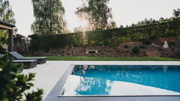 A swimming pool with a tiled deck, surrounded by a landscaped garden with a hedge and trees.