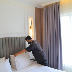 A hotel room with a bed, a nightstand, and a wall-mounted lamp. - Kala Hotel (Semarang)