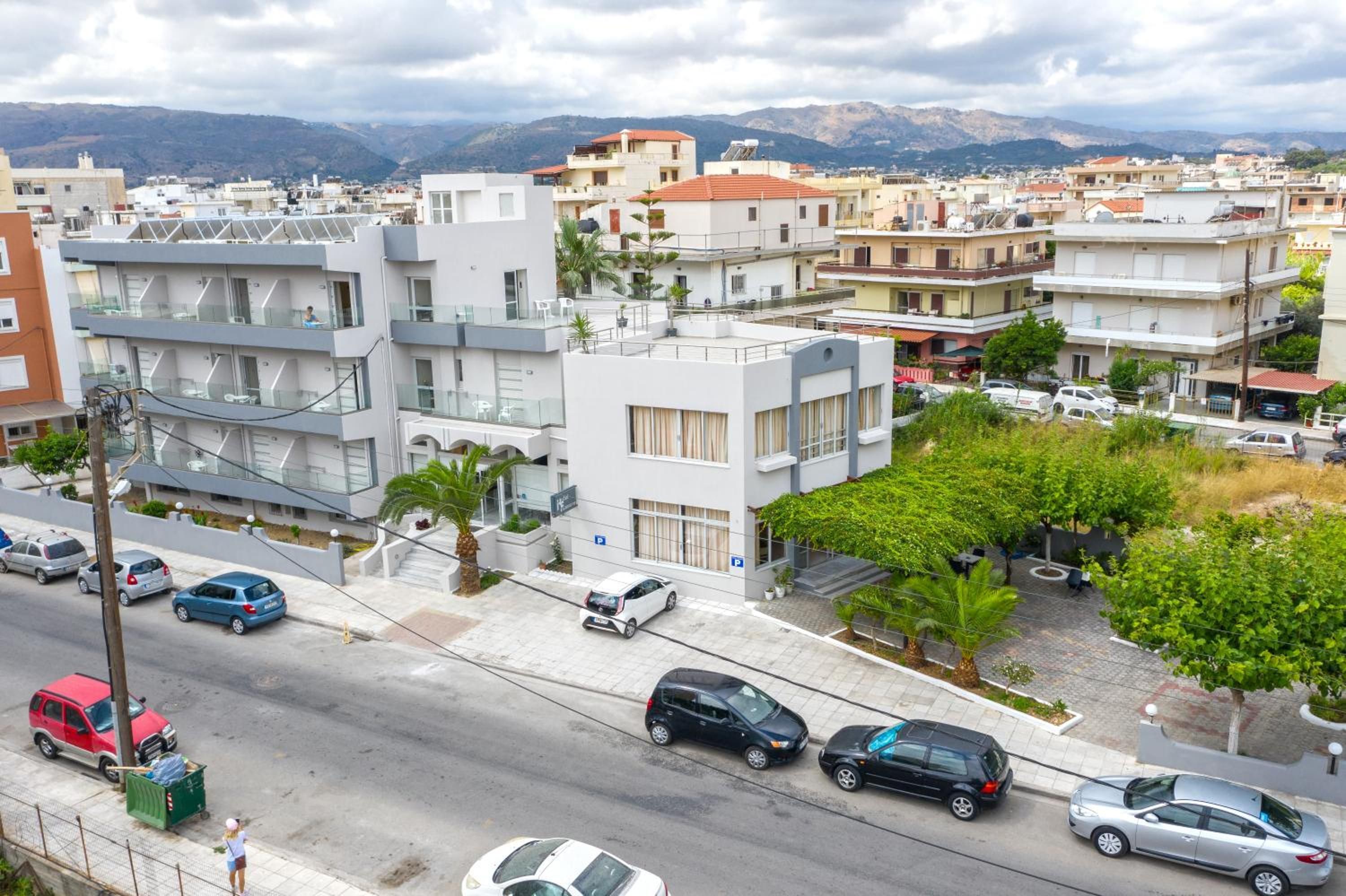A modern urban street with multi-story buildings, parked cars, and a clear view of distant mountains.
