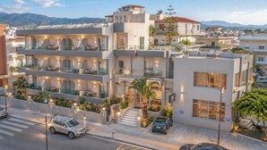 Un hotel de varios pisos con balcones, mobiliario exterior y una zona de estacionamiento.