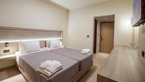 Una habitación de hotel con una cama, mesitas de noche, un televisor y una puerta que da a otra estancia.