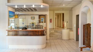 Zona de recepción de hotel con un mostrador curvo, una mesa de recepción, extintor, estatua y una puerta de madera.