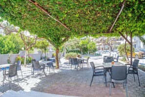 An outdoor café with tables and chairs under a pergola covered with greenery. - Falassarna Hotel (Chania)